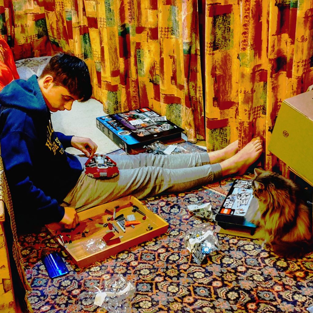 young man sitting with legs out on the floorbuilding a lego model in a living room