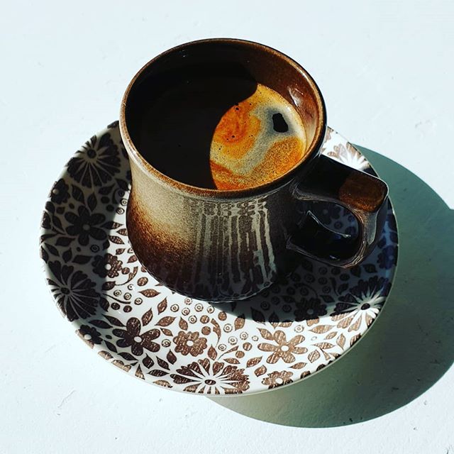 a brown cup fullof rich dark, black coffee on a white saucer with brown floral pattern.