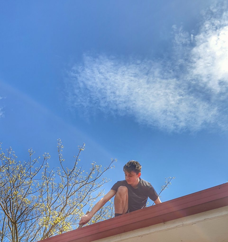 a young man on a roof cleaning out the gutters